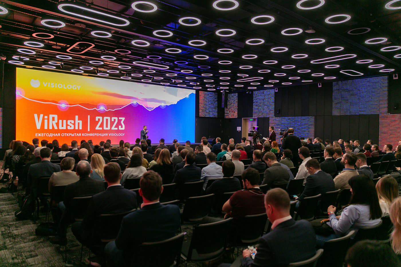 Полный зал ViRush 2023: экран конференции во всю стену, участники в креслах